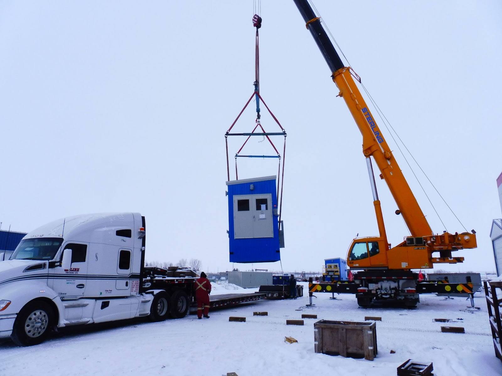 A Sterling crane lifting a blue piece of equipment by a truck