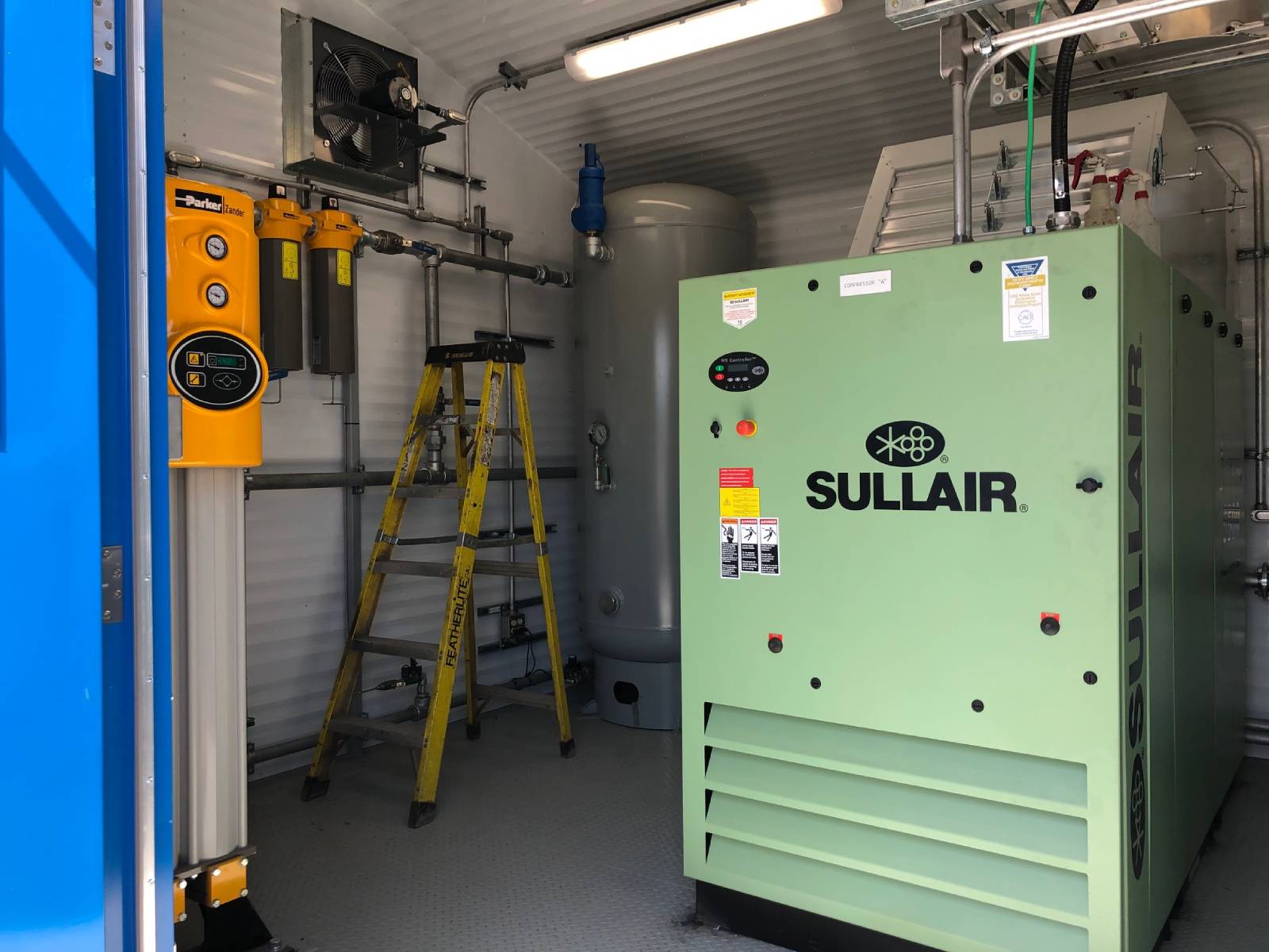 Inside view of an industrial equipment room with a green Sullair machine.