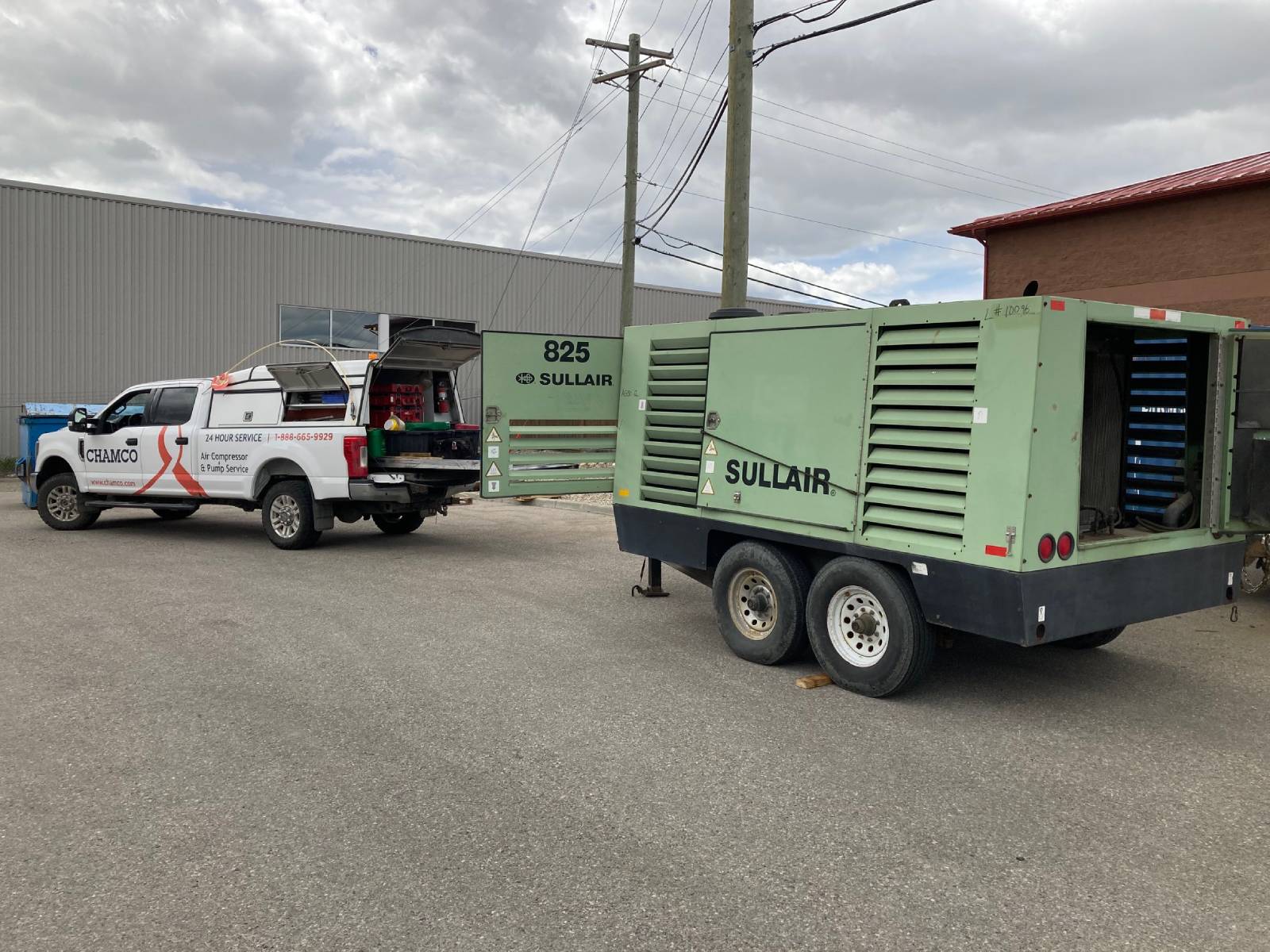 A white Chamco service truck parked next to a large green Sullair air compressor in an industrial area.