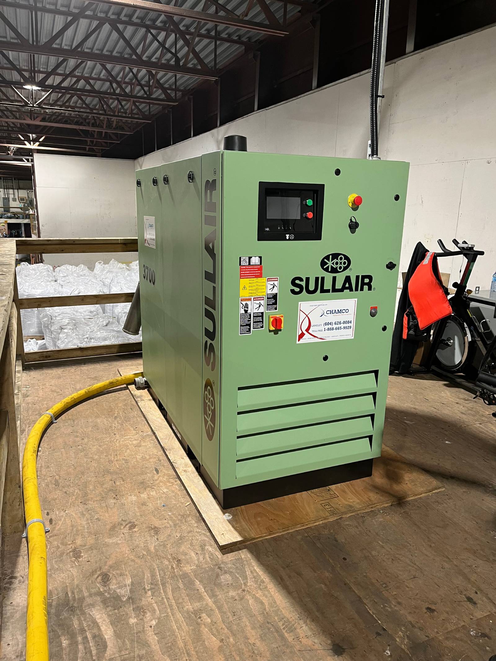 A Sullair industrial air compressor installed on a wooden platform at a fish farm, with a yellow hose connected for operation.