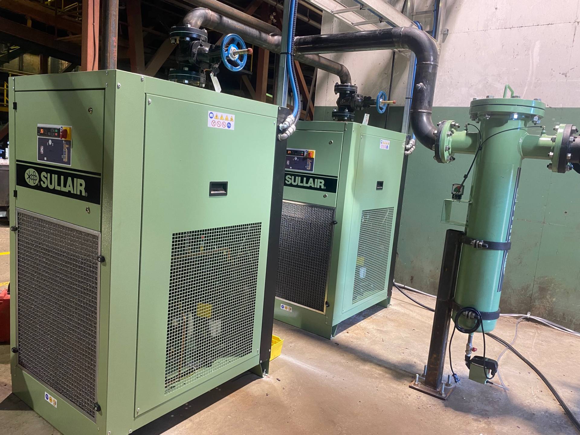 A pair of industrial air compressors located within a large warehouse environment, emphasizing the role of volumetric efficiency in optimizing system output.
