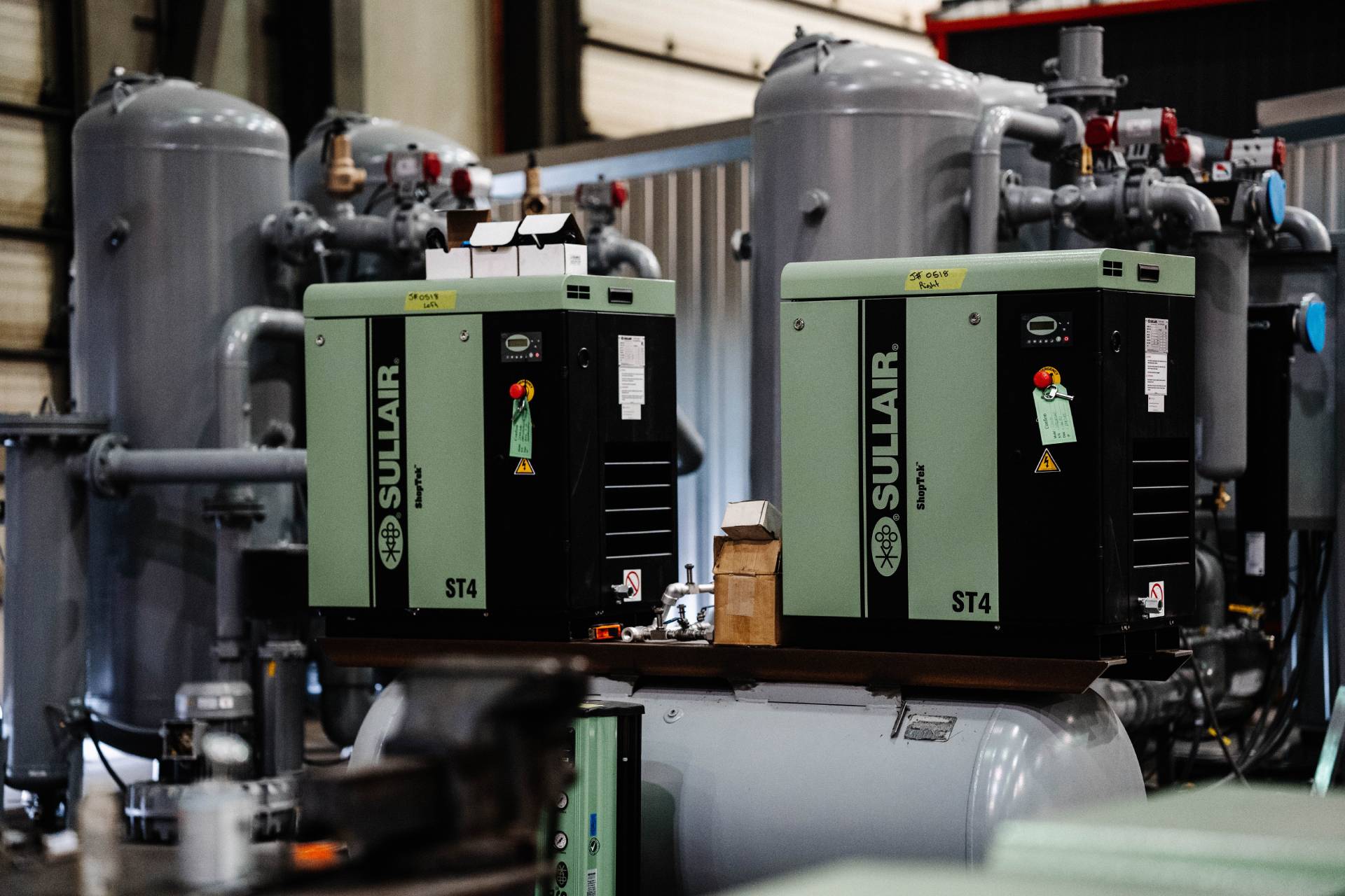 Sullair ST4 industrial air compressors in a facility, surrounded by piping and tanks, showcasing a typical setup for industrial compressed air systems.