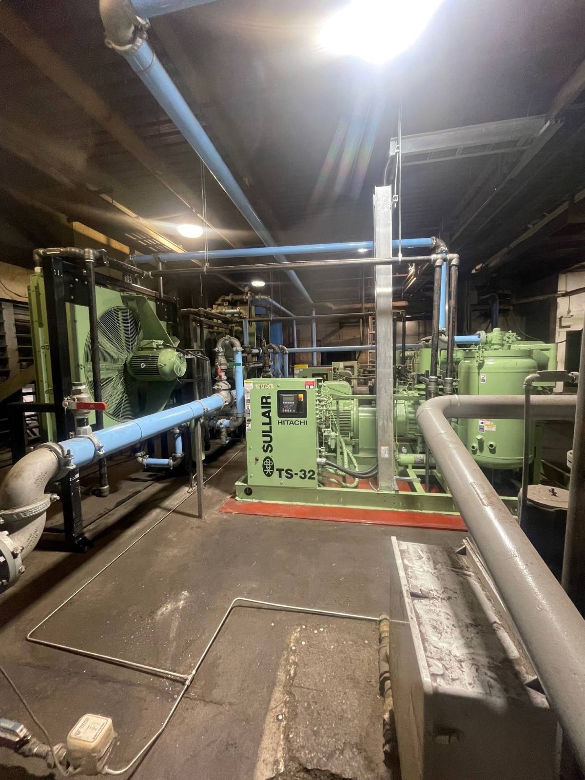 New-Sawmill-Compressed-Air-System Industrial compressor room housing a green Sullair TS32-350H air compressor with blue piping and overhead lighting, illustrating the custom compressed air system installed by Chamco at an Alberta sawmill.