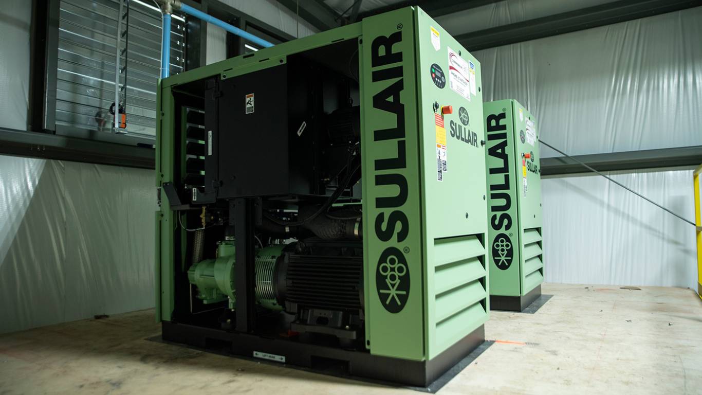 A Green Sullair industrial air compressor, installed indoors and shown from the front and side, to help illustrate common reasons compressors fail.