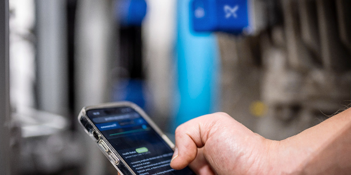 Maintenance technician using a smartphone to access cloud-based pump monitoring and diagnostics in an industrial facility.