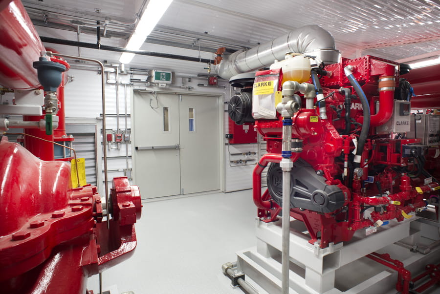 LNG_Fire_Pump_2-VMz80sjs Interior of a Chamco fire pump package showing diesel engines and red fire pumps with wide aisle clearance for stretcher access.