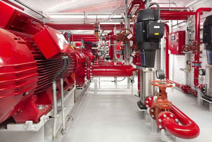 LNG_Fire_Pump_4-VMz80sjs Interior of a Chamco fire pump package showing large red electric motors, red piping, jockey pumps, and fire pump controllers, with a clear central aisle maintained throughout the length of the building.